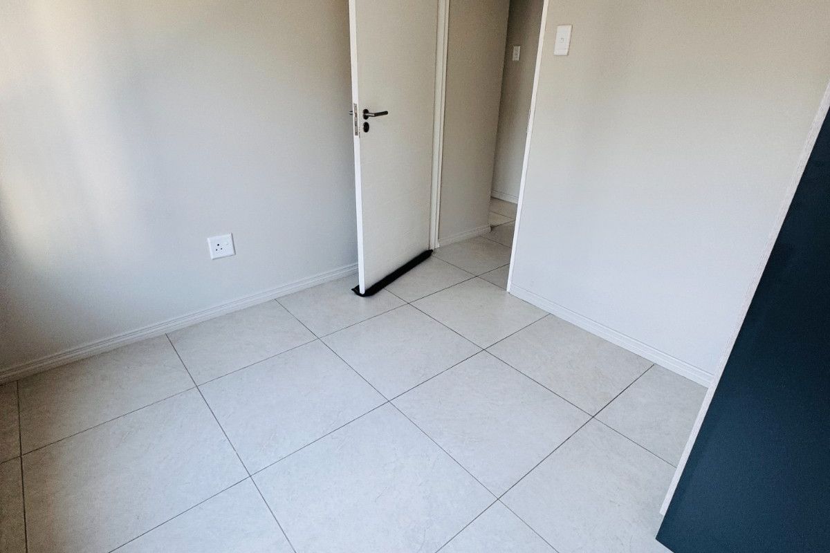 A clean, empty bedroom featuring neutral tiled flooring, smooth walls, and a doorway leading to an adjacent space.