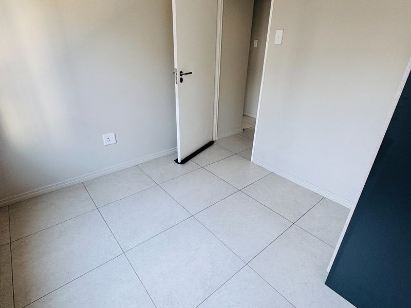 A clean, empty bedroom featuring neutral tiled flooring, smooth walls, and a doorway leading to an adjacent space.