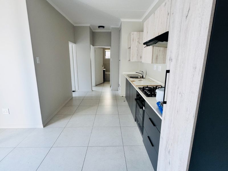 A modern, clean-lined kitchen featuring built-in cabinetry, a gas hob, and an electric oven, leading into a bright hallway with tiled flooring throughout.