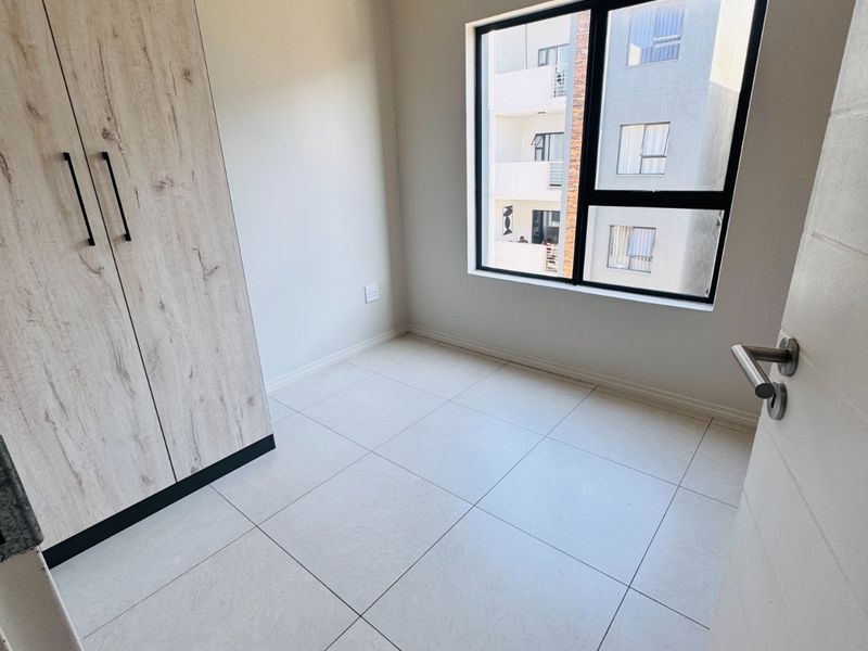 A bright, empty bedroom featuring modern tiled flooring and a built-in wardrobe with a light wood finish.