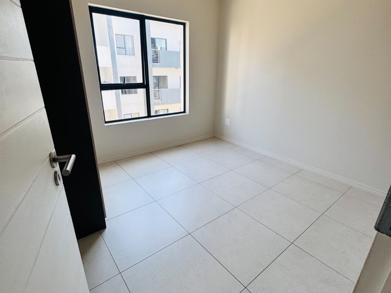 A bright, empty bedroom featuring neutral tiled flooring and a modern aluminium window frame, providing a clean canvas for interior design.