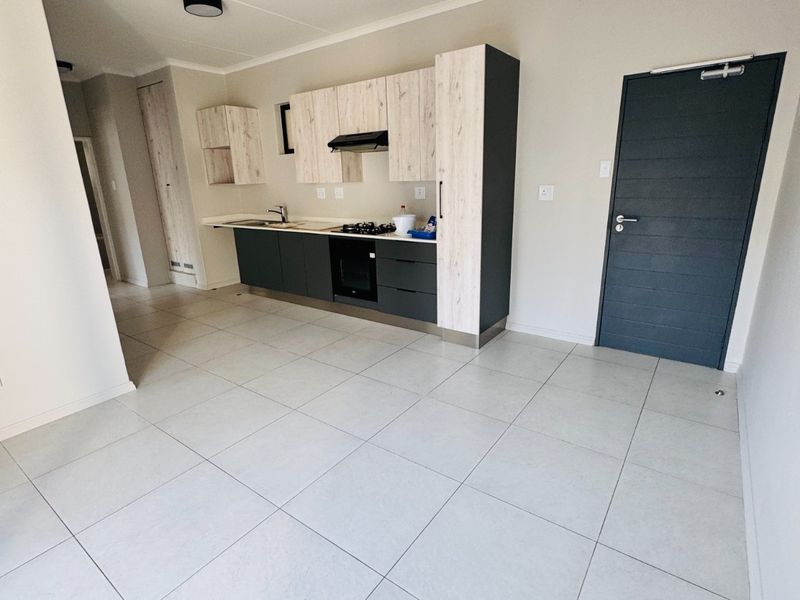Modern open-plan kitchen featuring two-tone cabinetry, built-in oven and hob, and neutral tiled flooring in a clean, vacant apartment space.