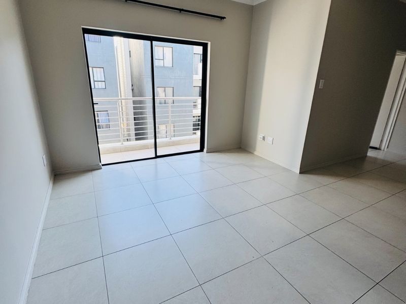 A bright, empty living area featuring neutral tiled flooring and a sliding glass door that opens onto a private balcony.