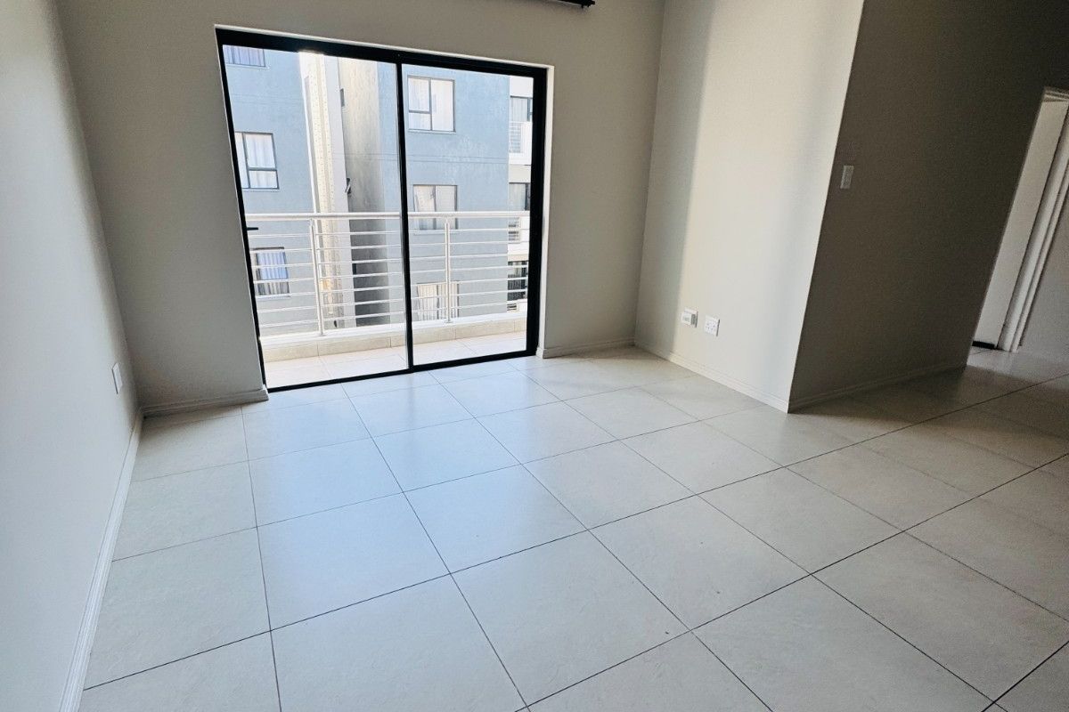 A bright, empty living area featuring neutral tiled flooring and a sliding glass door that opens onto a private balcony.