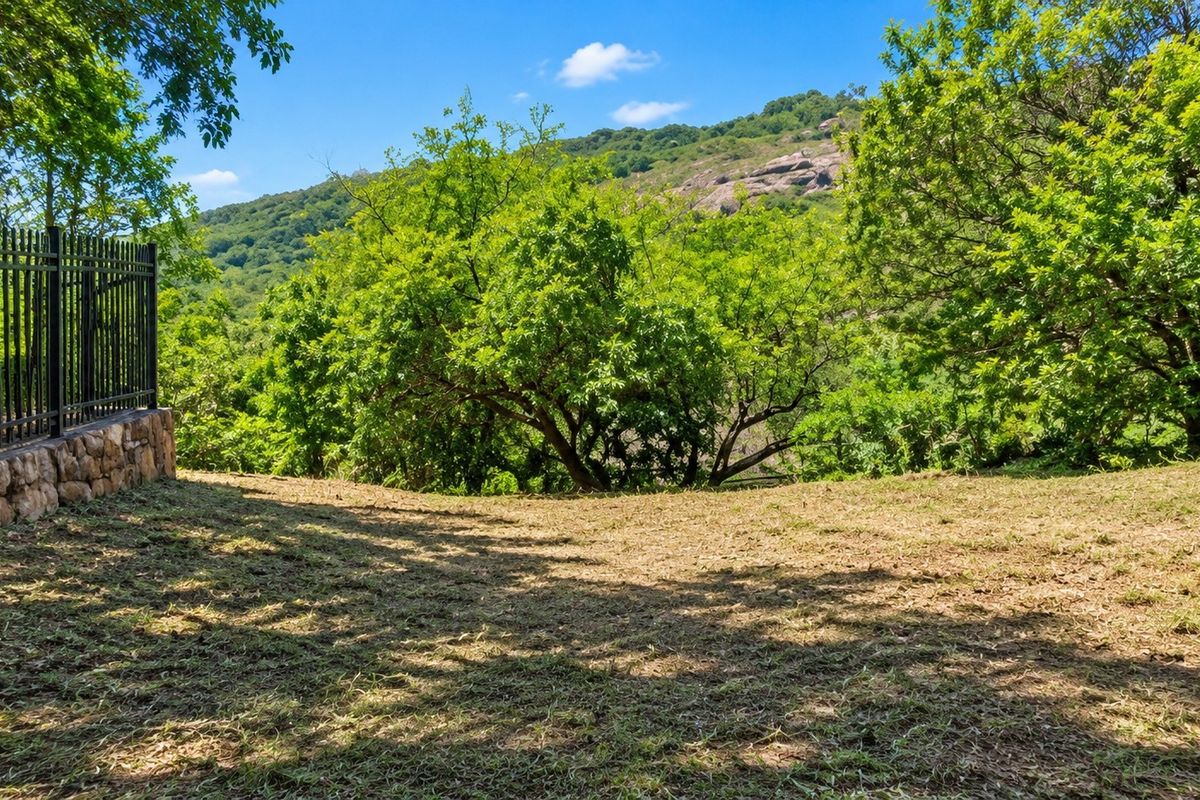 A scenic view of the surrounding landscape featuring a stone retaining wall and metal perimeter fencing on the property boundary.