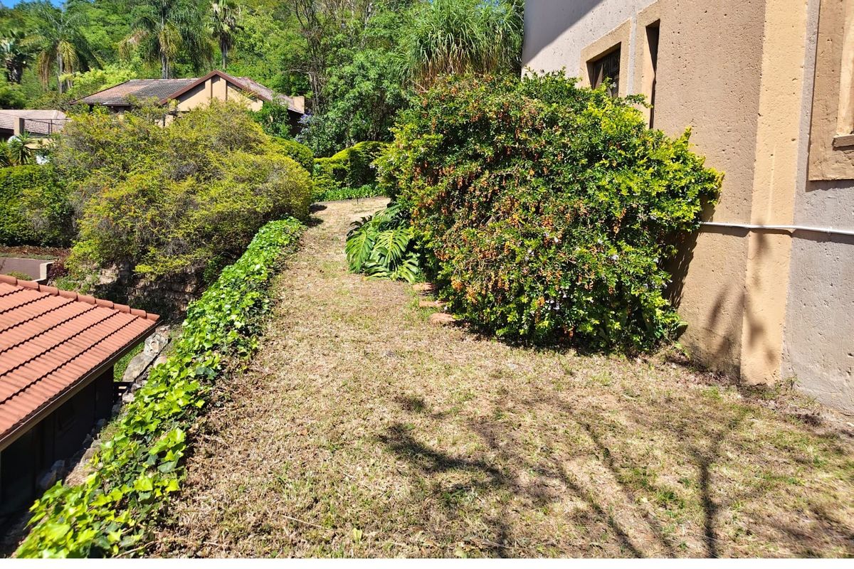 A view of the rear exterior area featuring a lawn, mature landscaping, and a portion of the building structure with a tiled roof.