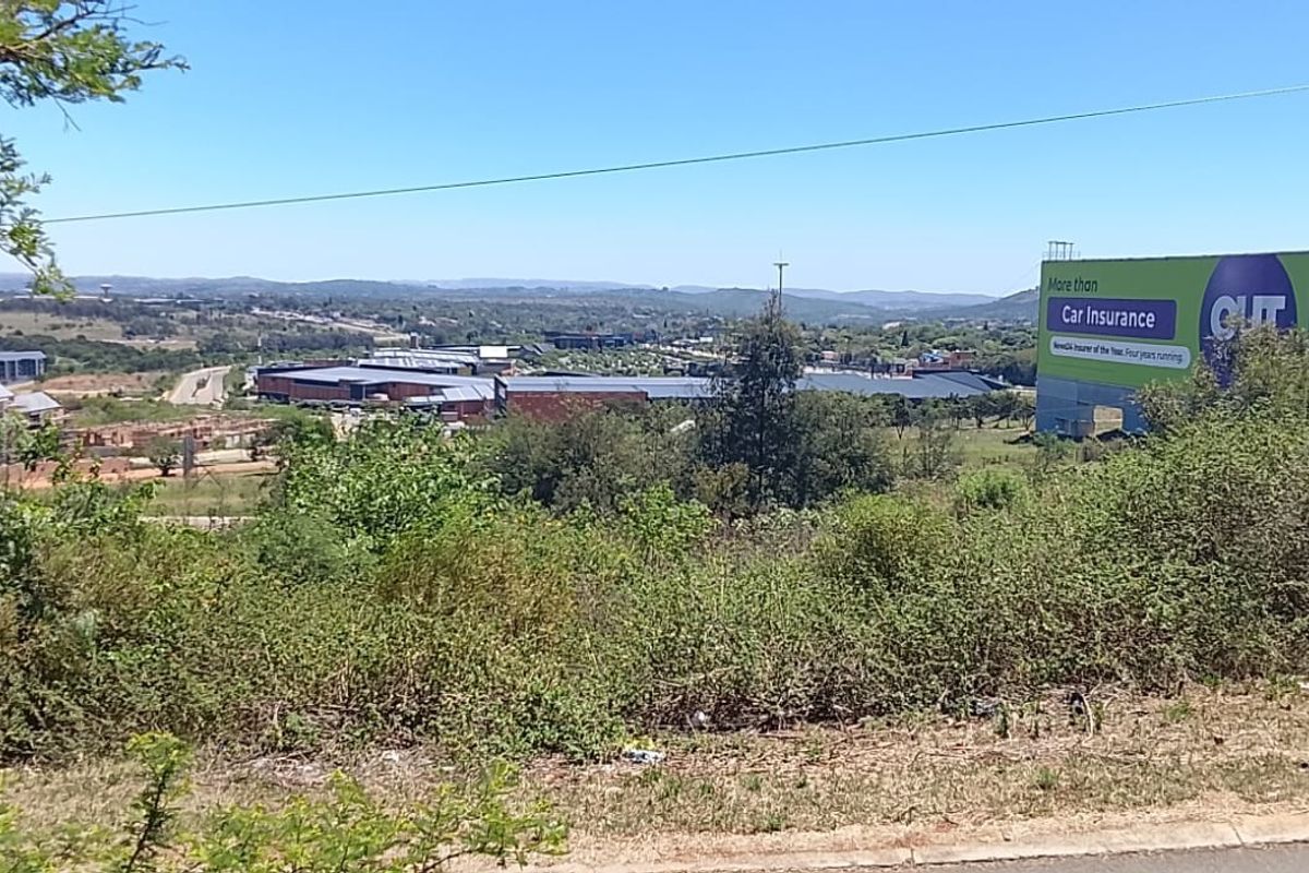 Elevated view overlooking a residential area and commercial development, featuring natural vegetation and a large roadside billboard.