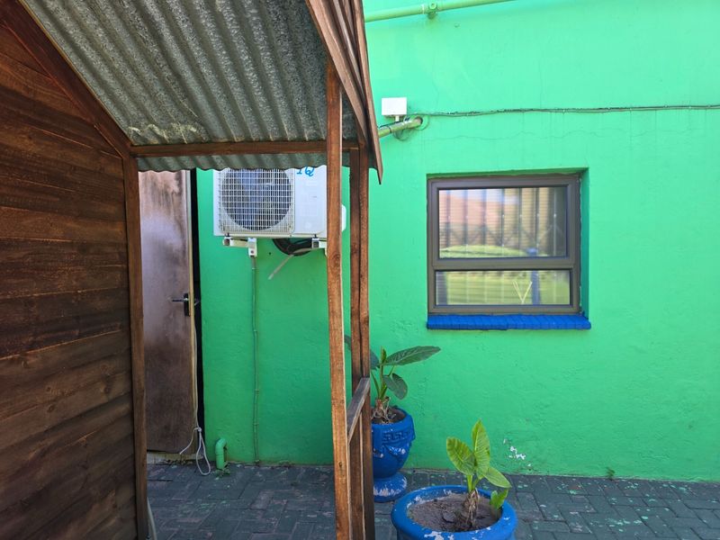 Rear exterior area featuring a paved courtyard, a timber structure, and a bright green wall with an installed air conditioning unit.