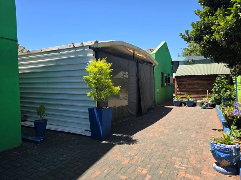 A rear courtyard area featuring paved flooring, a corrugated metal structure, a timber shed, and an external air conditioning unit.