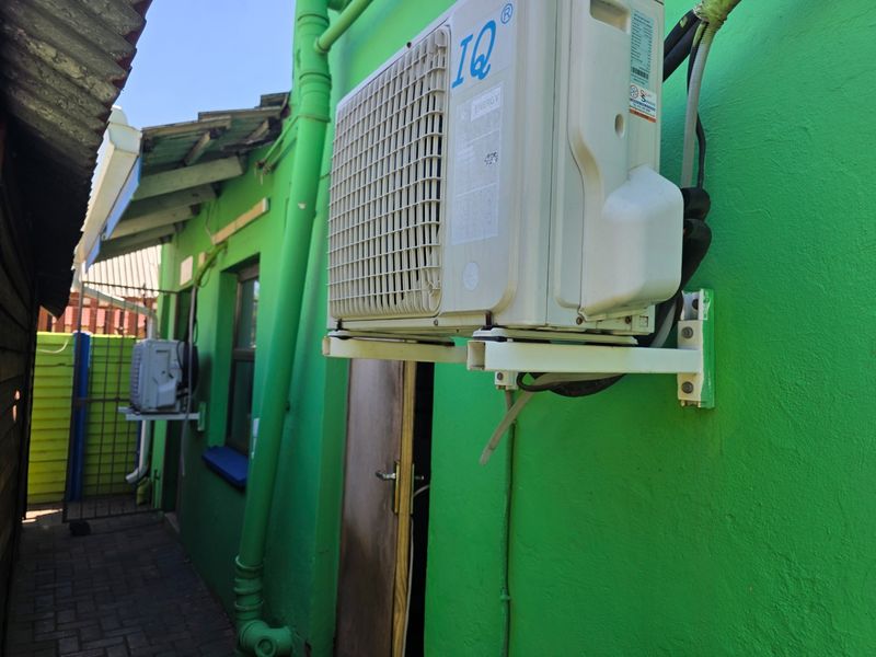 A side exterior view of the office building featuring wall-mounted air conditioning units, a paved walkway, and an external access door.
