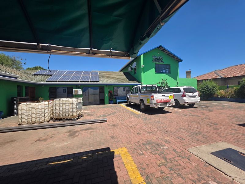 Front exterior view of the office building featuring a paved parking area, solar panel installation, and green facade with signage.