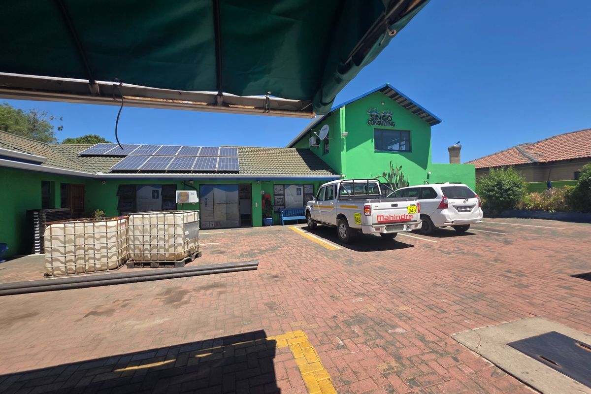 Front exterior view of the office building featuring a paved parking area, solar panel installation, and green facade with signage.