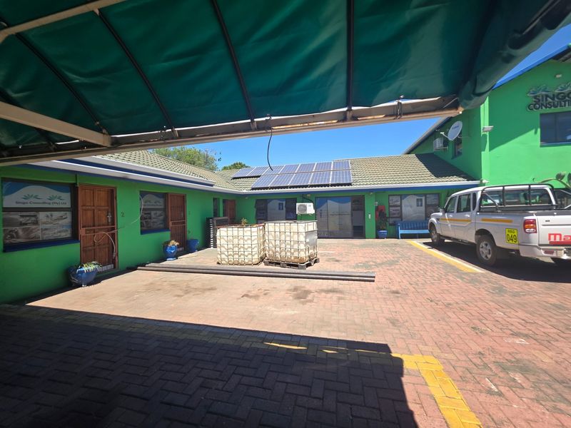 Rear exterior view of the office property featuring a paved courtyard, solar panel installation, and covered parking area.