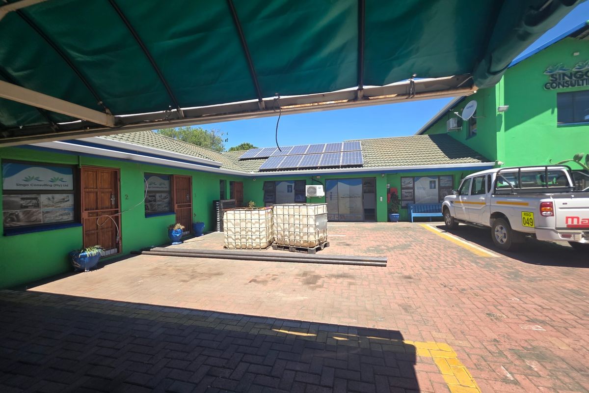 Rear exterior view of the office property featuring a paved courtyard, solar panel installation, and covered parking area.