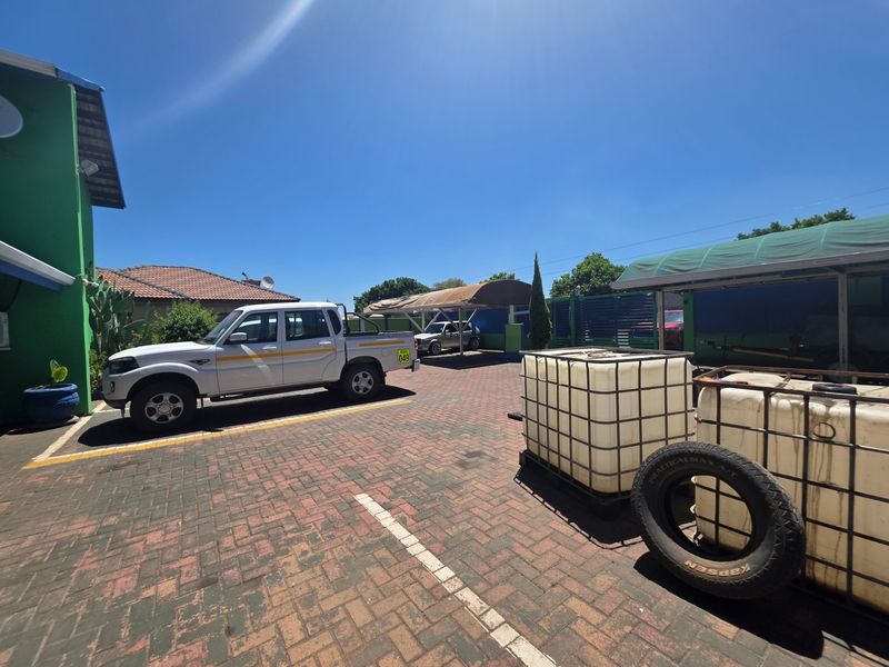 A paved outdoor parking area featuring a carport structure and perimeter fencing, suitable for office vehicle storage.