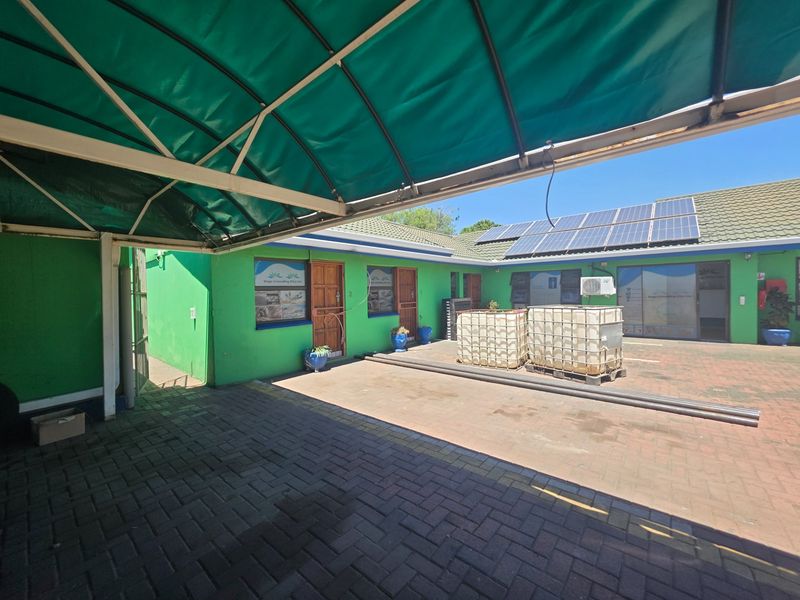 Rear exterior courtyard featuring a paved area, covered parking structure, solar panel installation, and multiple office access points.
