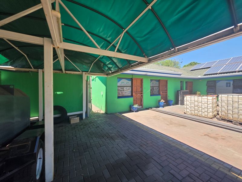 Rear exterior view of the office property featuring a paved driveway, covered carport, and roof-mounted solar panels.