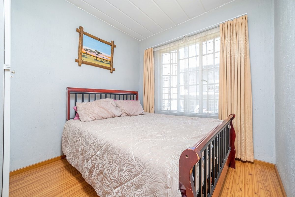 A functional bedroom featuring laminate flooring, a window with security bars, and a tongue and groove ceiling.