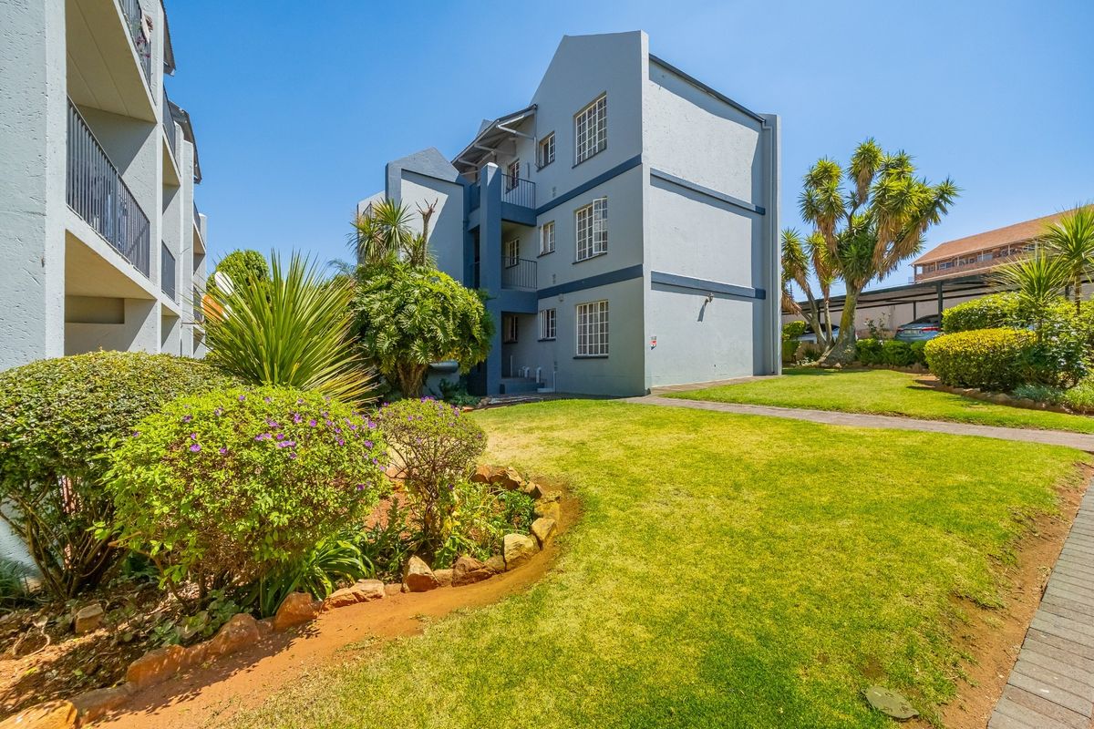 A view of the apartment building exterior featuring a well-maintained garden, paved walkways, and multi-story residential units with balconies.