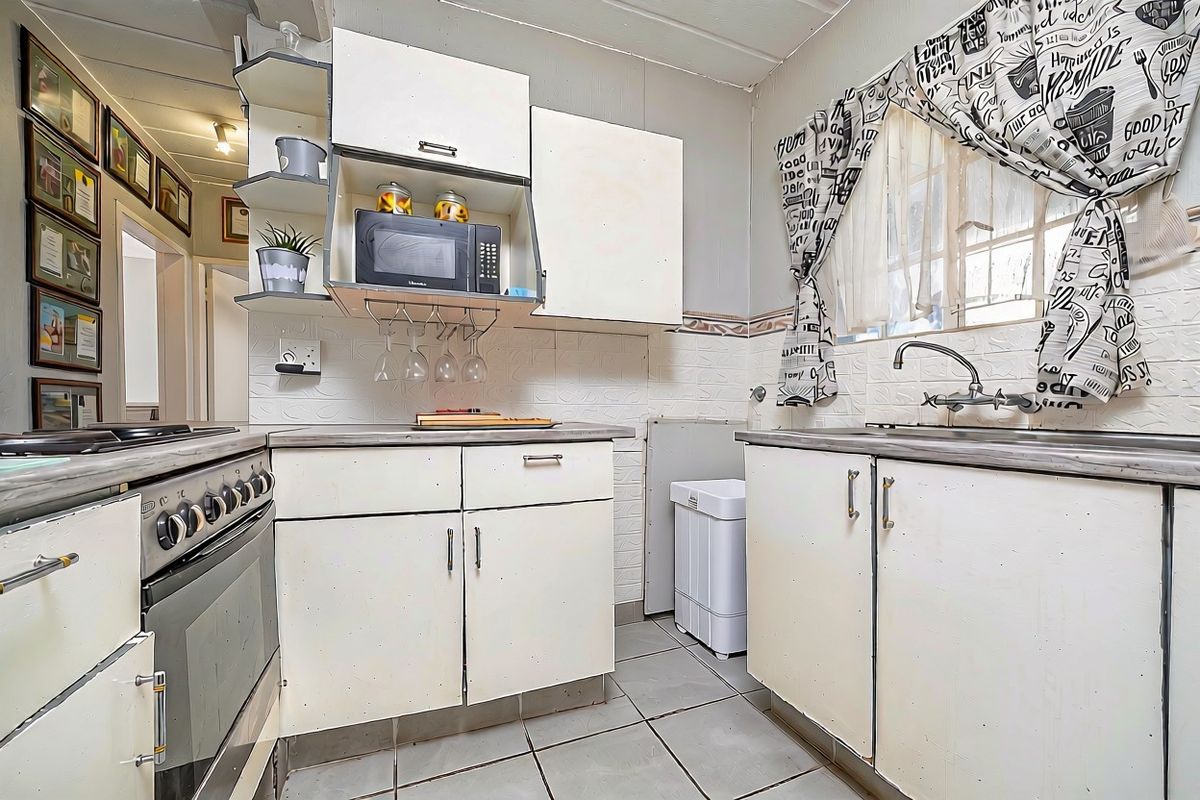 A compact kitchen featuring built-in cabinetry, a stainless steel sink, and a built-in oven with hob, offering a functional layout with dated finishes.