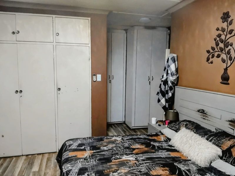 A bedroom featuring built-in cupboards and laminate flooring, offering functional storage space with potential for cosmetic updates.