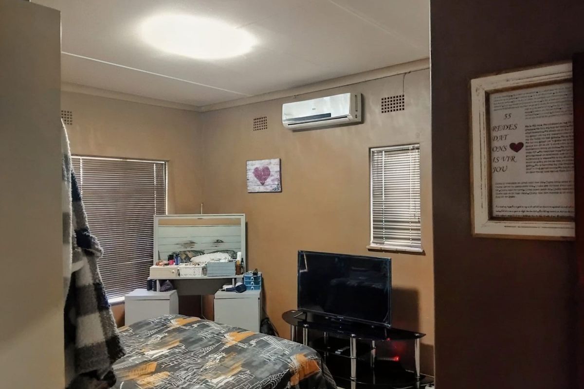A bedroom featuring laminate flooring, venetian blinds, and a wall-mounted split-system air conditioner.