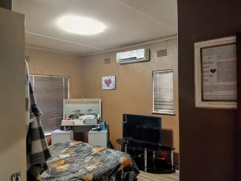 A bedroom featuring laminate flooring, venetian blinds, and a wall-mounted split-system air conditioner.