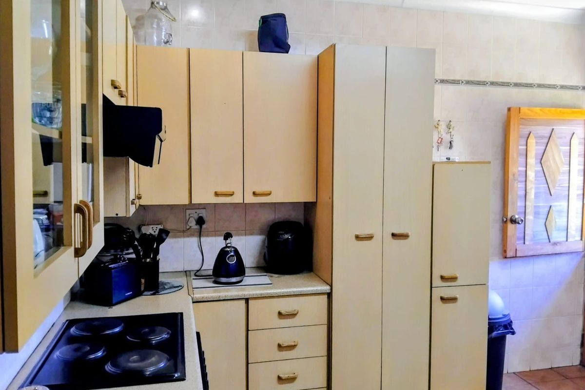 A functional kitchen featuring built-in cabinetry, laminate countertops, and an electric hob with tiled backsplash and flooring.