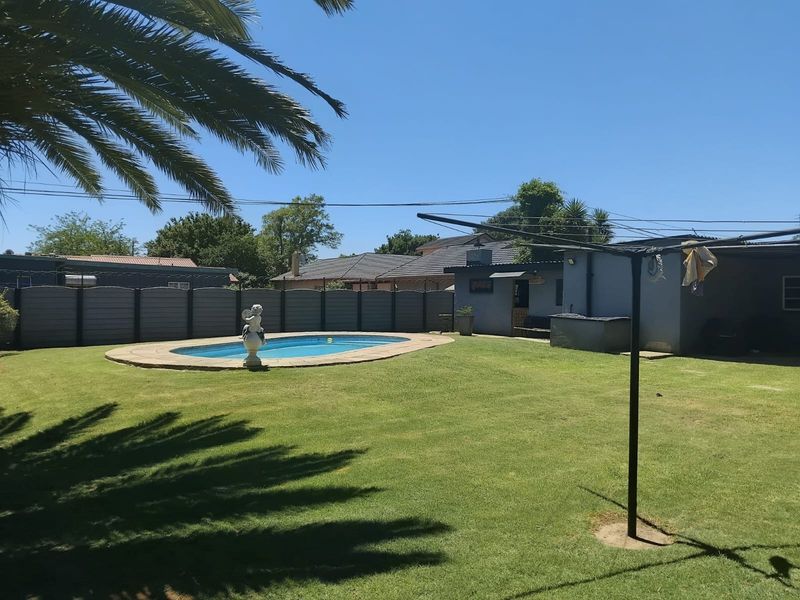 A spacious backyard featuring a swimming pool, well-maintained lawn, perimeter fencing, and a detached outbuilding.