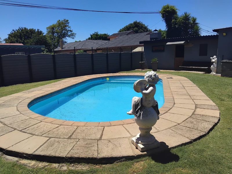 Outdoor pool area featuring a swimming pool with a paved surround, set within a private garden enclosed by a precast concrete boundary wall.