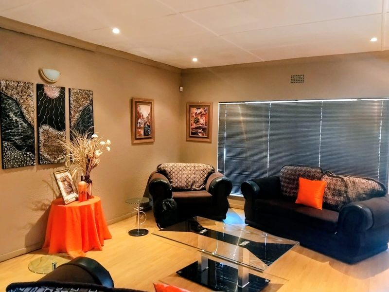 A comfortable living room featuring laminate flooring, recessed downlighting, and large windows fitted with venetian blinds.