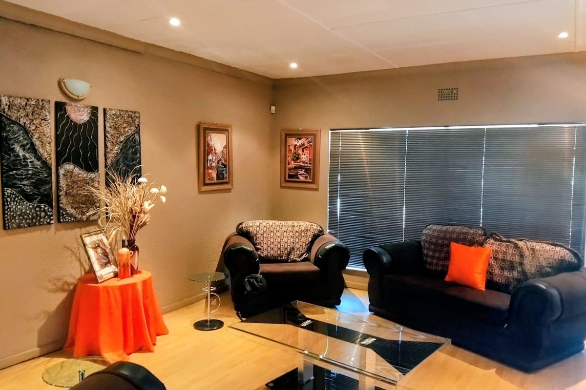 A comfortable living room featuring laminate flooring, recessed downlighting, and large windows fitted with venetian blinds.