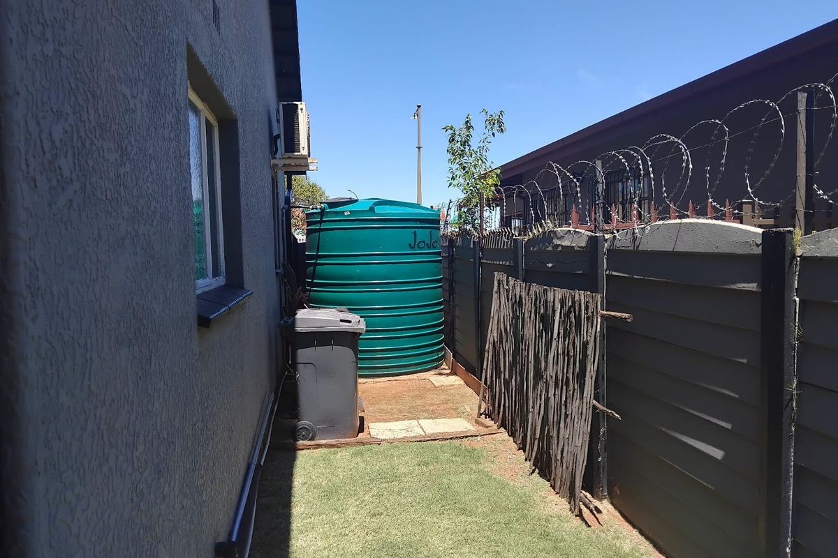 Side yard area featuring a water storage tank, precast boundary wall with security razor wire, and an external air conditioning unit.