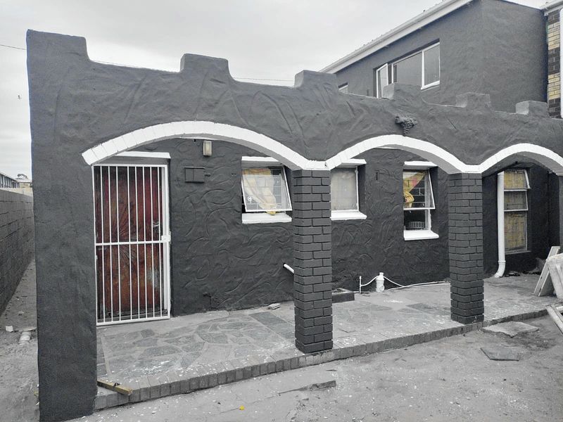 A covered patio area featuring arched masonry columns, stone paving, and security access, currently requiring final landscaping and finishing touches.
