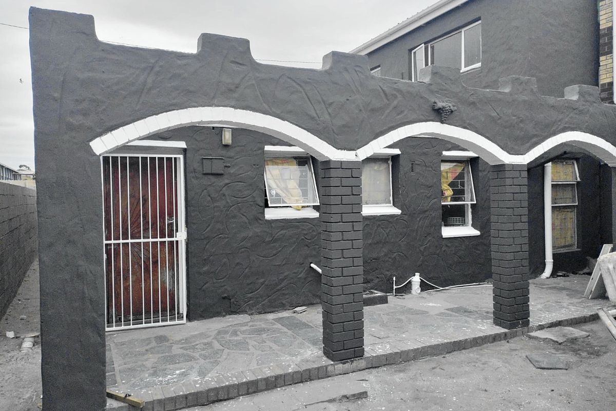 A covered patio area featuring arched masonry columns, stone paving, and security access, currently requiring final landscaping and finishing touches.