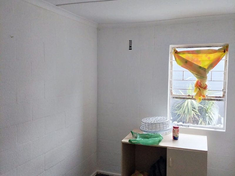 A simple, vacant bedroom featuring tiled flooring, security bars on the window, and a basic ceiling light fixture.