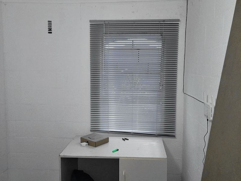 A small, unfinished bedroom space featuring tiled flooring, venetian blinds, and exposed electrical wiring, requiring cosmetic updates and finishing.