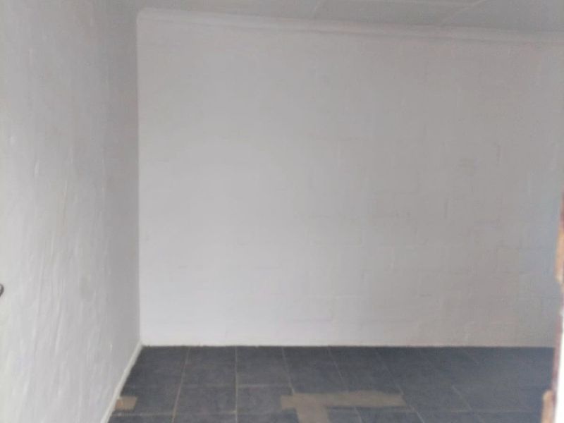 An empty utility space featuring tiled flooring and a simple ceiling light fixture, suitable for storage or a workshop area.