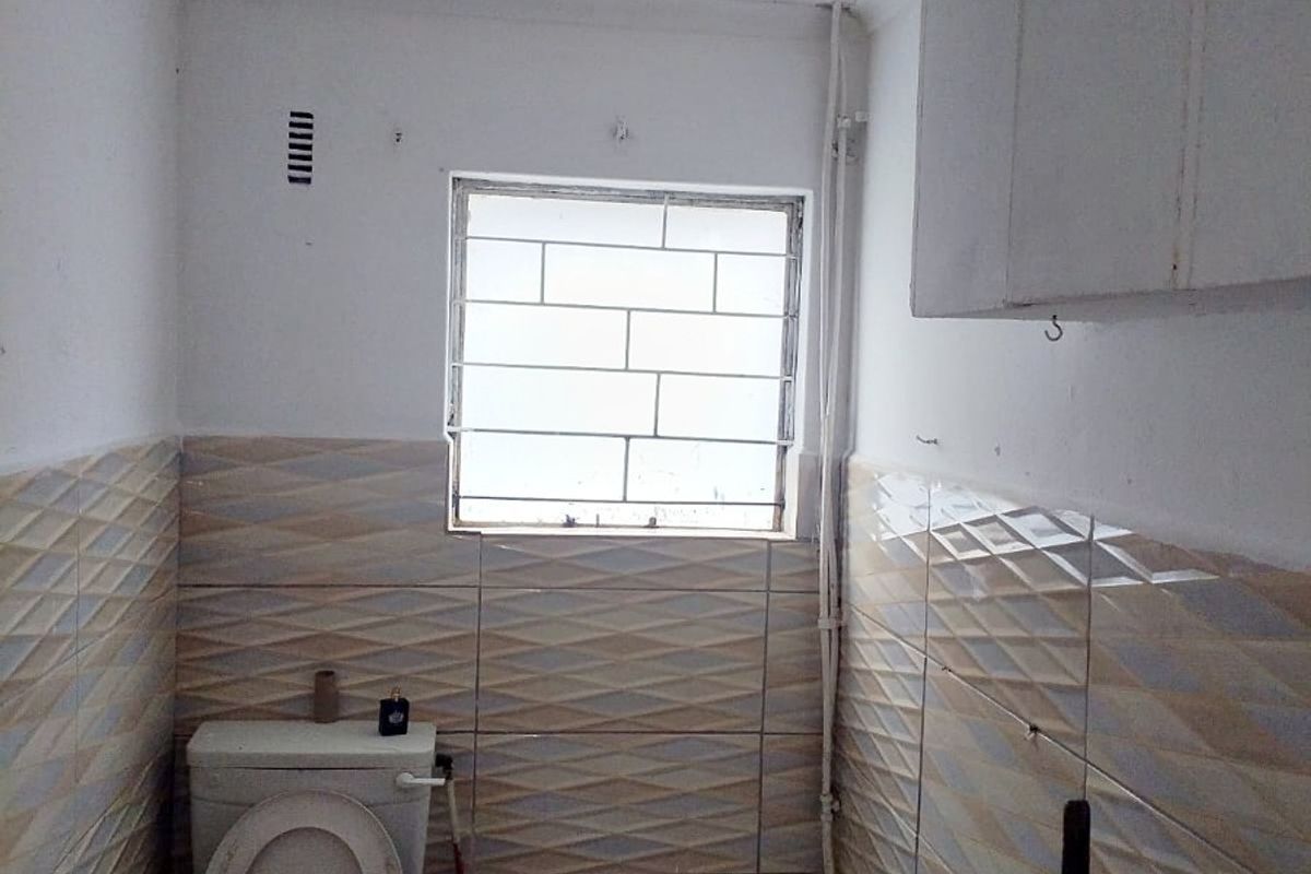 A compact bathroom featuring a bathtub, toilet, and wall-mounted storage cabinet, finished with patterned wall tiles and security bars on the window.