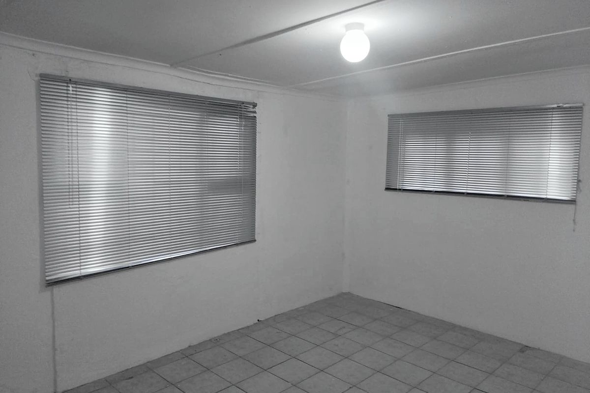An empty bedroom featuring tiled flooring, venetian blinds, and a simple ceiling light fixture, offering a blank canvas for renovation.
