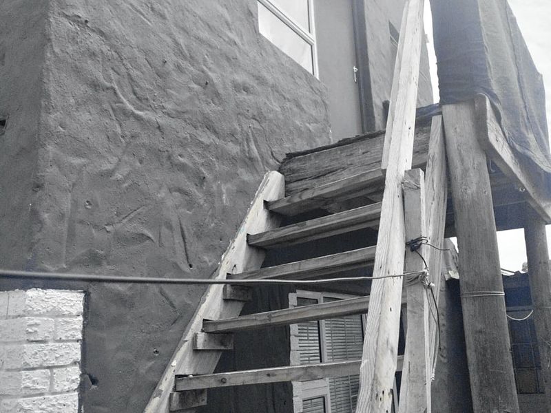Exterior view of a rear building elevation featuring a weathered wooden staircase leading to a raised timber deck area.