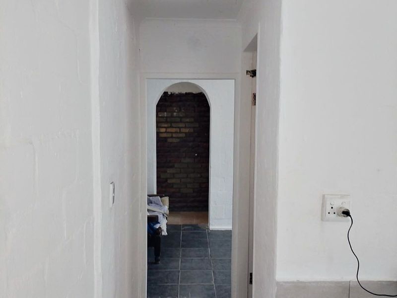 A narrow hallway featuring dark floor tiles, white painted walls, and an arched doorway leading to an area with exposed brickwork.