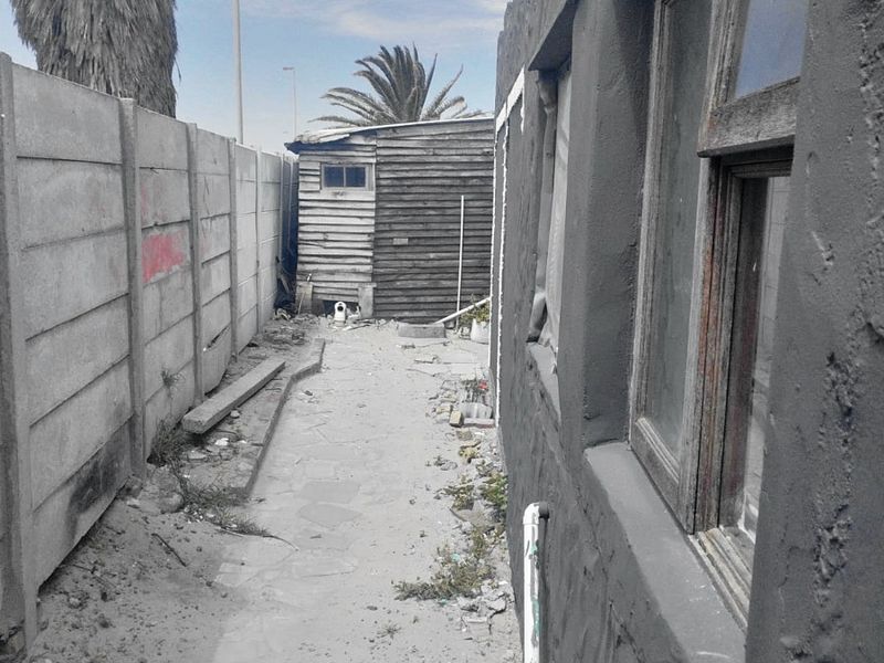 A narrow rear exterior side passage featuring a precast concrete boundary wall, a timber shed, and weathered exterior wall finishes requiring maintenance.