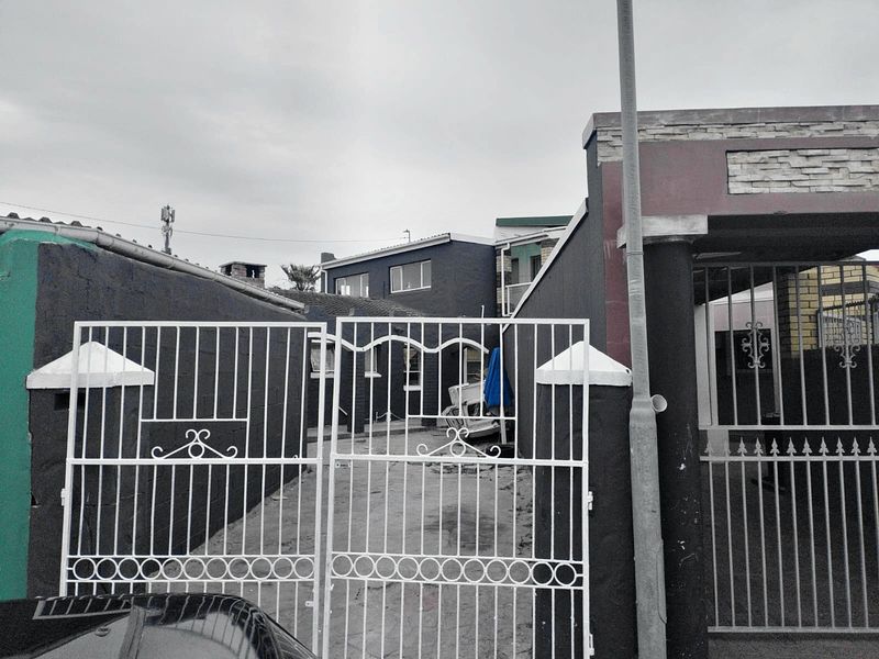 Front view of the property featuring a metal security gate, concrete driveway, and boundary wall with stone cladding accents.
