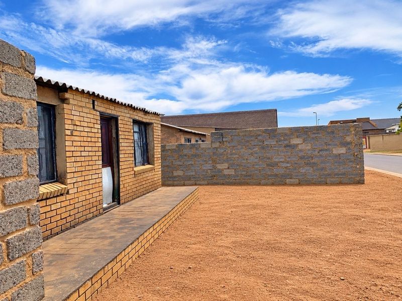 Exterior view of a face brick house featuring a paved walkway and an unfinished concrete block boundary wall on a large, undeveloped plot.