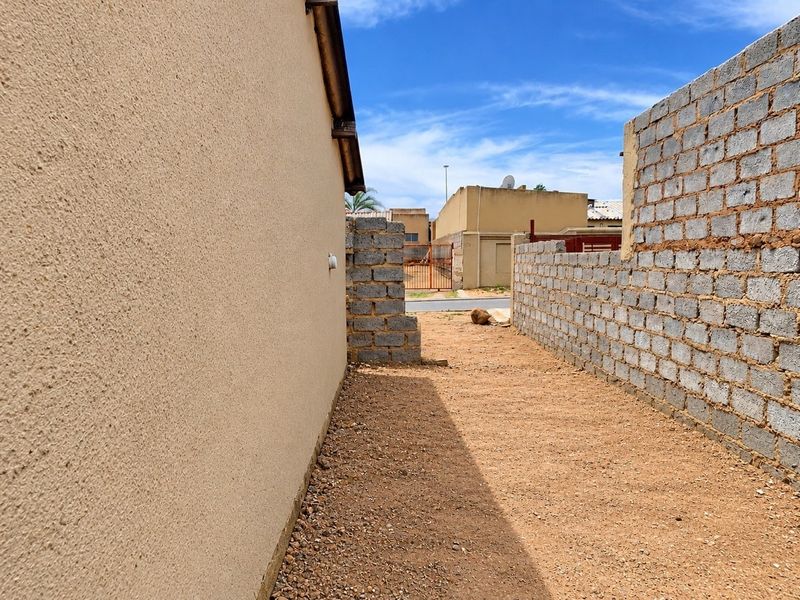 A side yard area featuring a textured exterior wall and an unfinished concrete block boundary wall with a gravel ground surface.