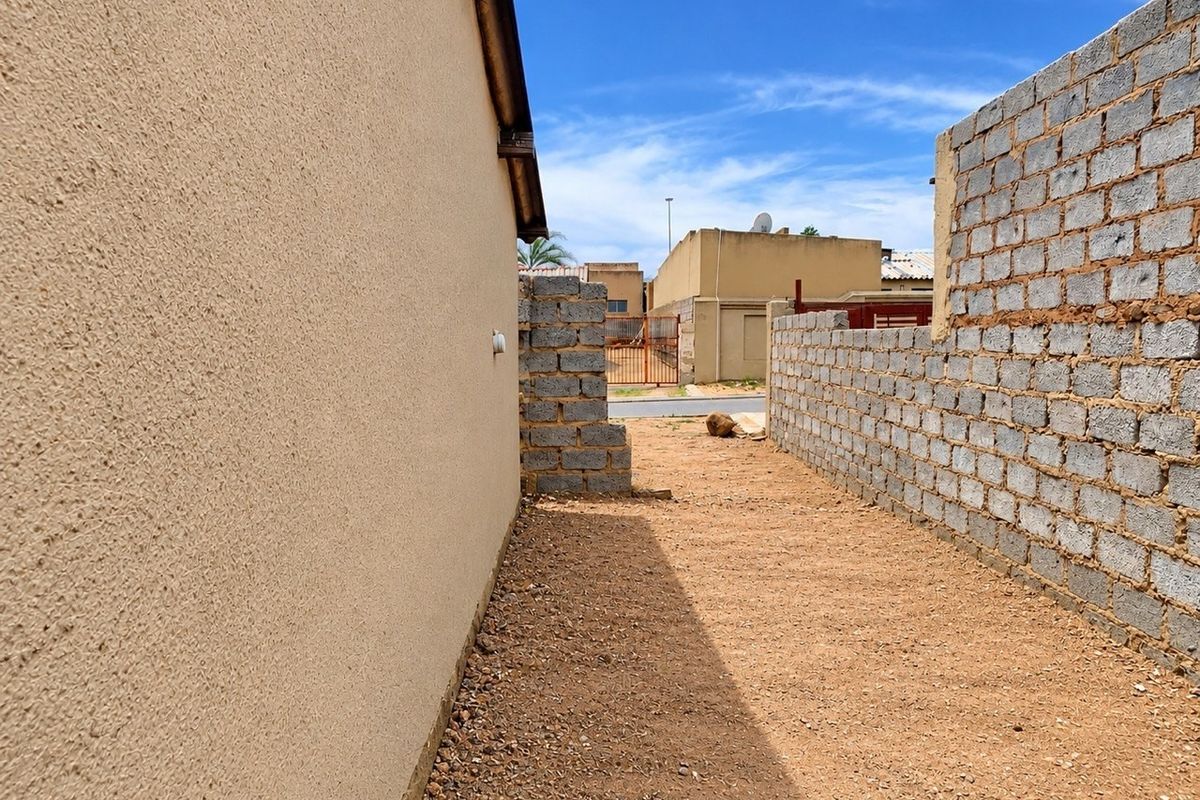 A side yard area featuring a textured exterior wall and an unfinished concrete block boundary wall with a gravel ground surface.