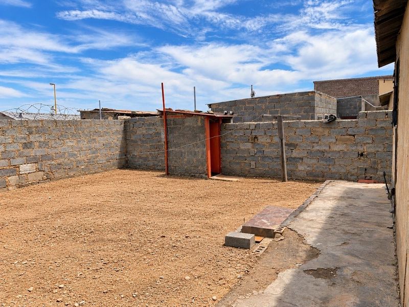 A spacious rear yard featuring a concrete block boundary wall, paved walkway, and an external utility structure, offering potential for landscaping and outdoor improvement.