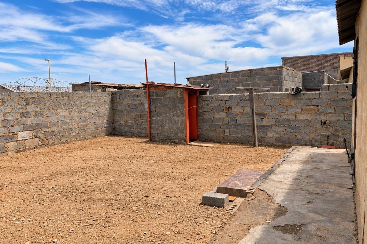 A spacious rear yard featuring a concrete block boundary wall, paved walkway, and an external utility structure, offering potential for landscaping and outdoor improvement.