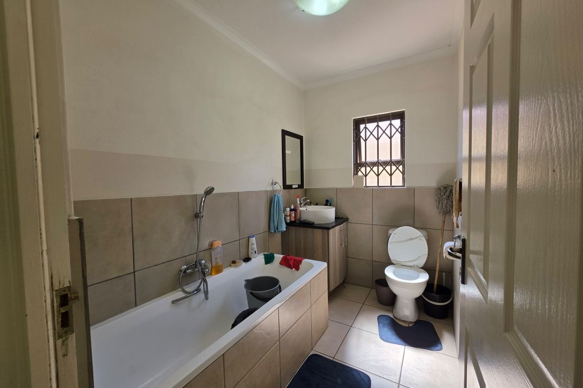 A functional bathroom featuring a bathtub with shower mixer, a vanity cabinet with vessel sink, and a toilet, finished with neutral wall and floor tiles.